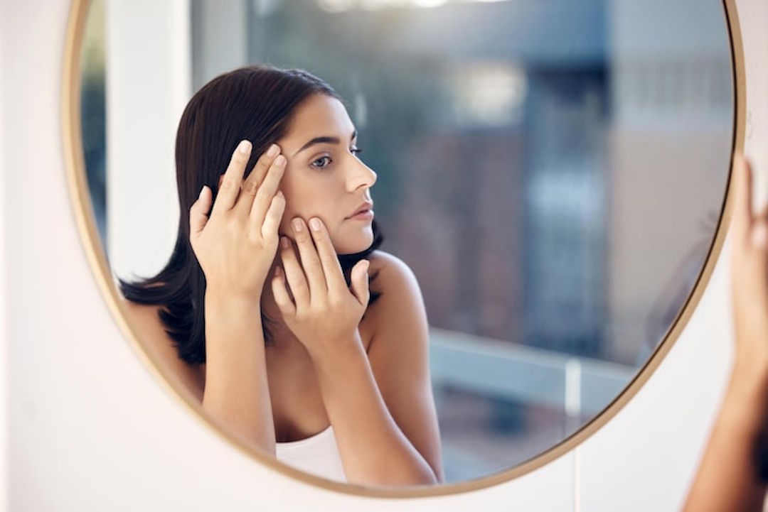 Une femme qui regarde ses acnés sur son visage dans un miroir