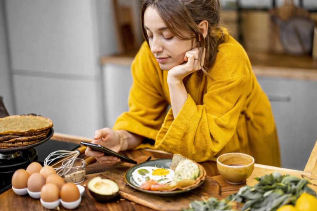 une femme européenne qui mange un oeuf sur plat dans sa cuisine