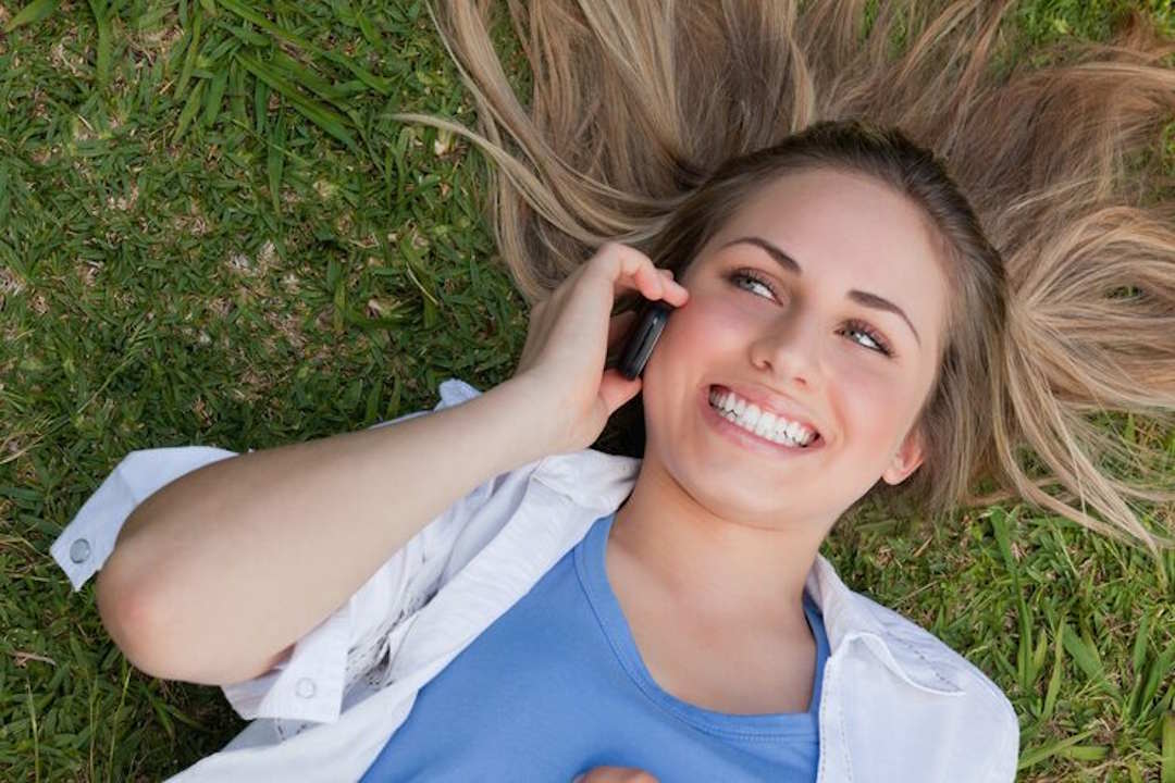 Une femme au téléphone qui sourit avec de belles dents grâce au clcium