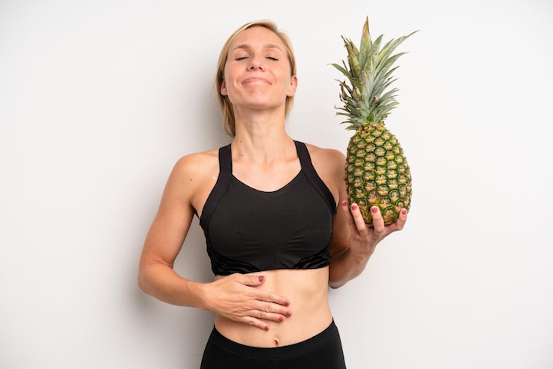 Une femme qui se tient le ventre et un ananas dans une main