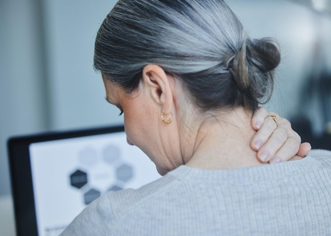 Une femme qui se tient le cou à cause d'une douleur d'arthrose cervicale