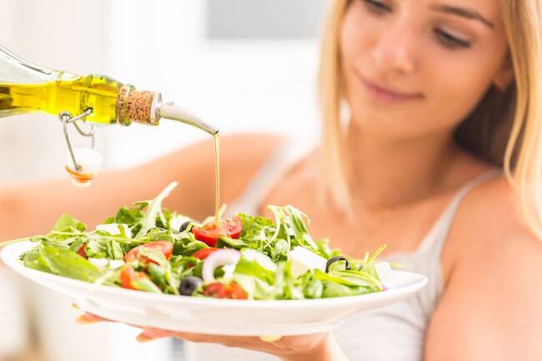 Une femme qui verse de l'huile d'olive dans une salade