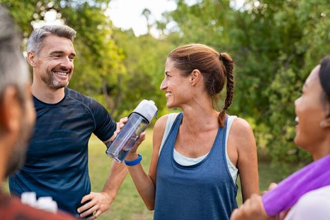 Un groupe de sportif qui discutent en souriant et en buvant de l'eau