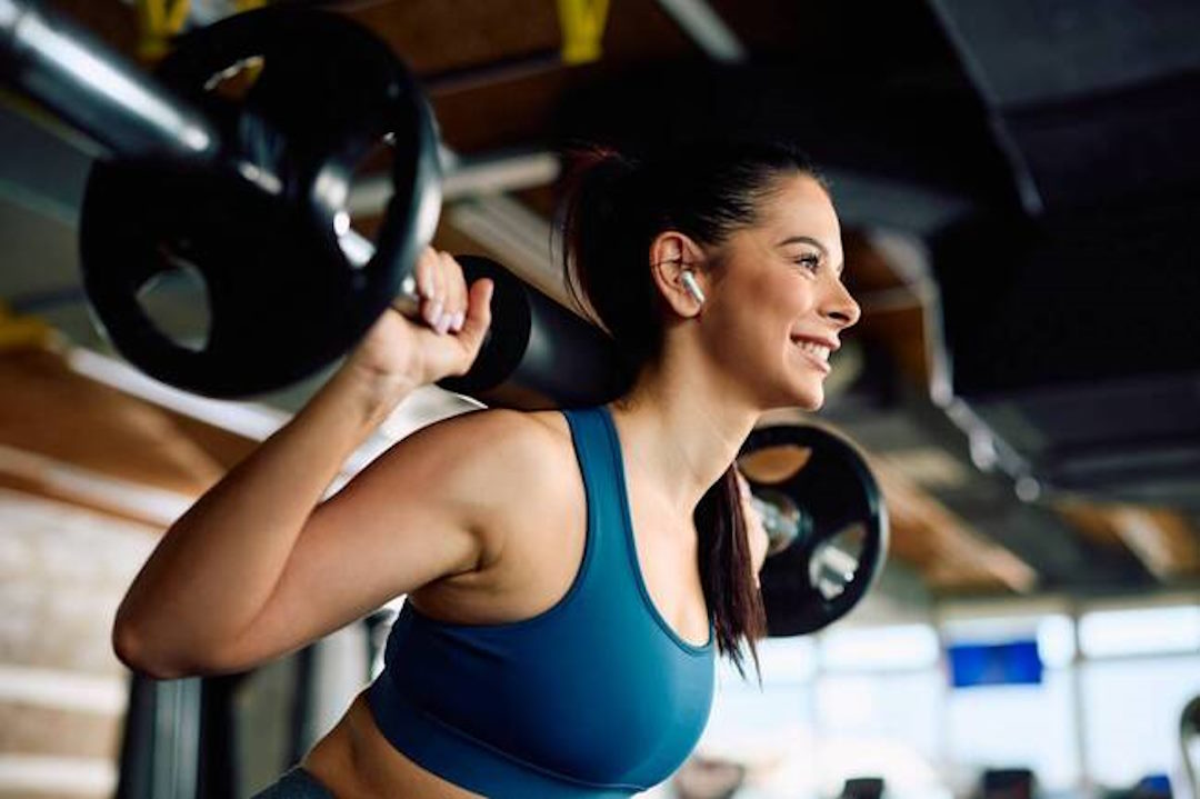 Une femme au salle de sport qui fait du squat avec des barres sur les épaules