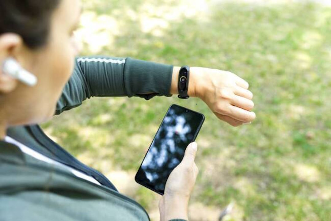 Une femme qui mesure ses performances pendant une course à pieds avec un smartphone et une montre connectée