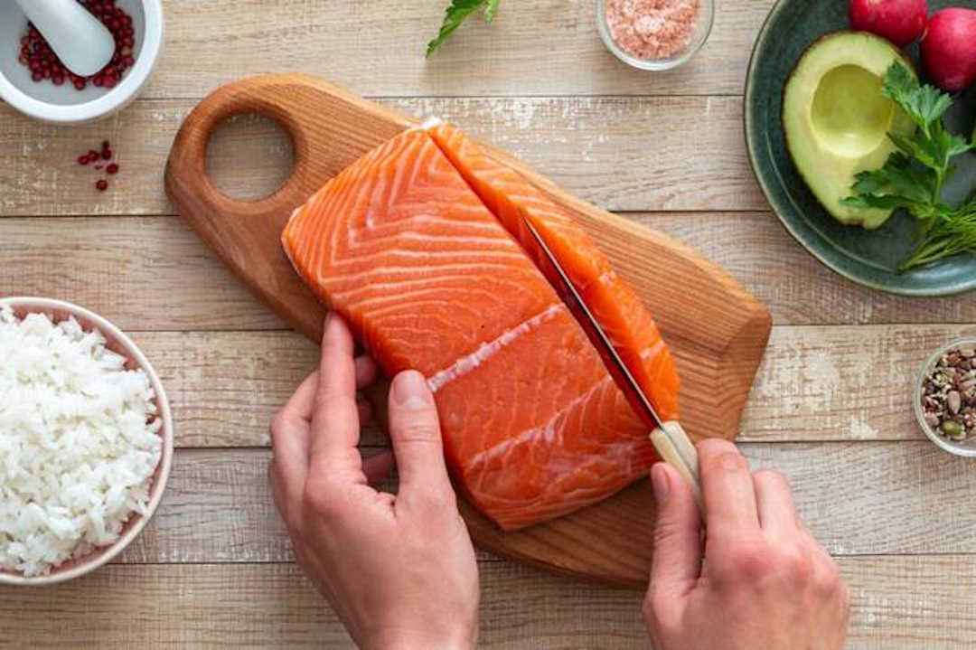 Une main qui tranche du saumon sur un plateau