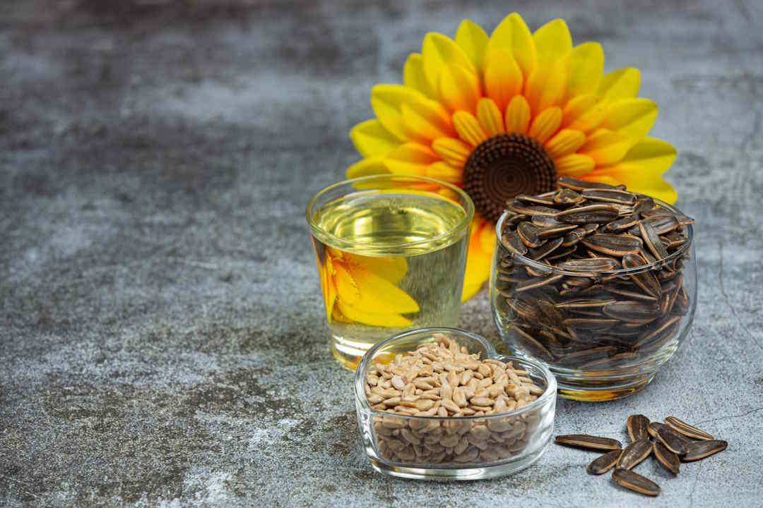 Des graines de tournesol posé à côté d'huile de tournesol et d'une fleur