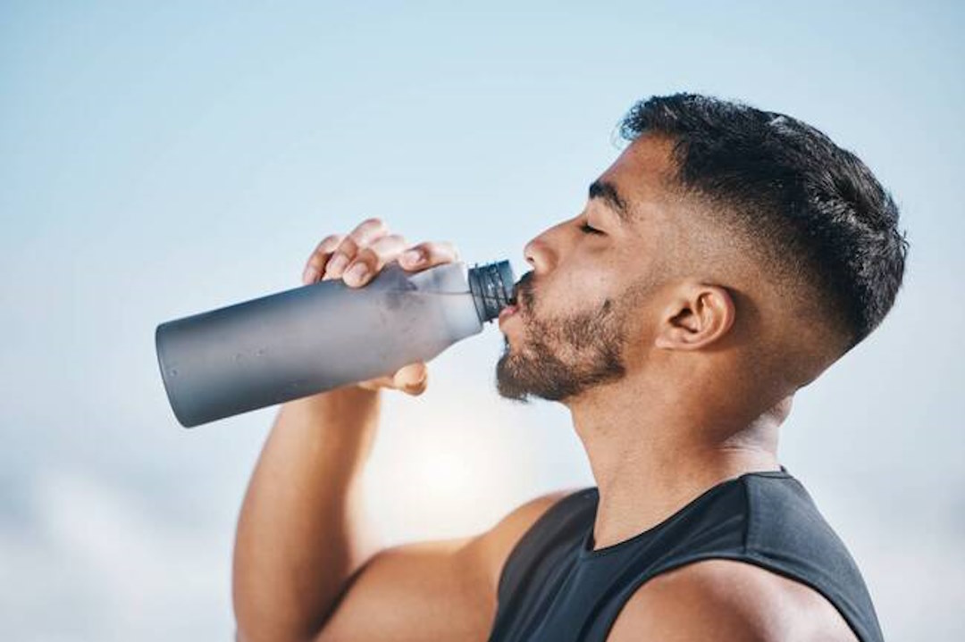 Un homme qui boit de l'eau, bien s'hydrater pendant les activités physiques