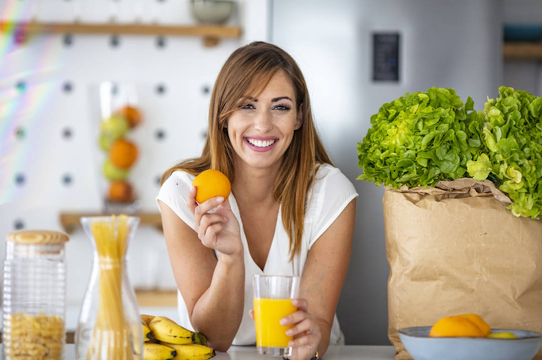 Une femme qui tient un orange et un verre de jus d'orange 